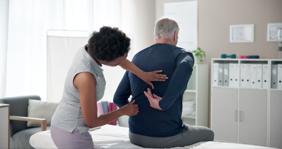 Senior, man and physiotherapist with consultation for back pain in clinic with healthcare or injury treatment on bed. Physical therapy, medical expert or mature patient with massage or rehabilitation