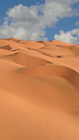 Flying over endless yellow sand dunes in desert. Sand dunes and blue sky with clouds. Aerial view of Beautiful desert landscape, Vertical Video