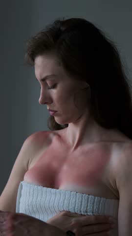 A woman examines her red, sunburned chest, indicating pain and discomfort from prolonged sun exposure