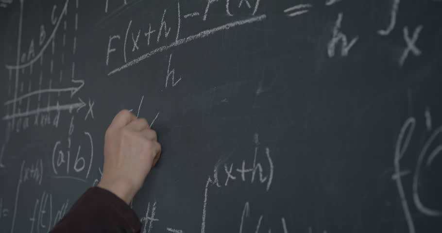 Close-up of male hand writing mathematics formula on chalkboard while professor working at theory in classroom. Education and science concept.