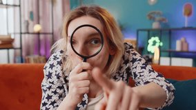 Investigator researcher scientist Caucasian young woman holding magnifying glass near face looking into camera with big zoomed funny eye searching analyzing. Surprised girl sitting at home room sofa. - Powered by Shutterstock - Get 15% off with code: PIKWIZARD15