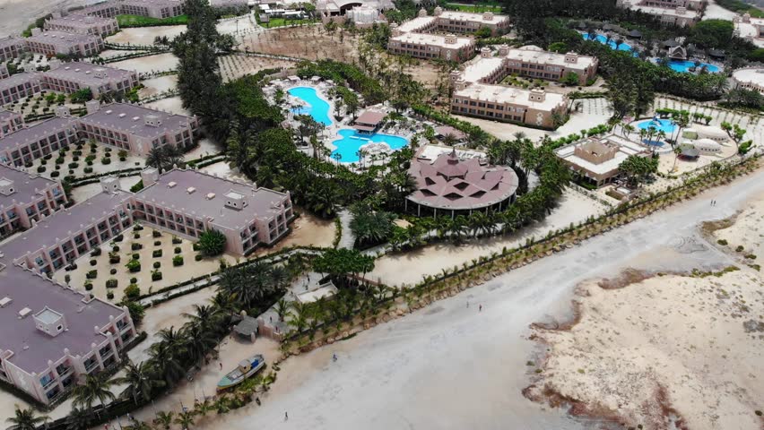 Aerial footage of the Hotel Riu Palace Cabo Verde Cape Verde showing the swimming pools and holiday makers relaxing and sunbathing in the sun next to the swimming pools on a beautiful sunny day