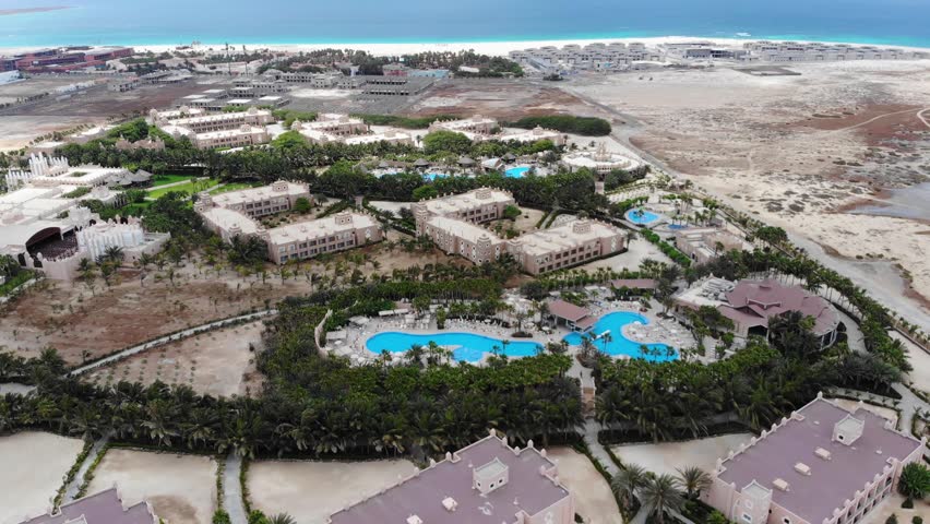 Aerial footage of the Hotel Riu Palace Cabo Verde Cape Verde showing the swimming pools and holiday makers relaxing and sunbathing in the sun next to the swimming pools on a beautiful sunny day