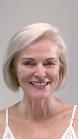 Close up portrait: face of old happy smiling woman. Senior female in the white studio laughing. Mature middle aged lady with positive emotion looking at camera. Pensioner retiree lifestyle, emotions