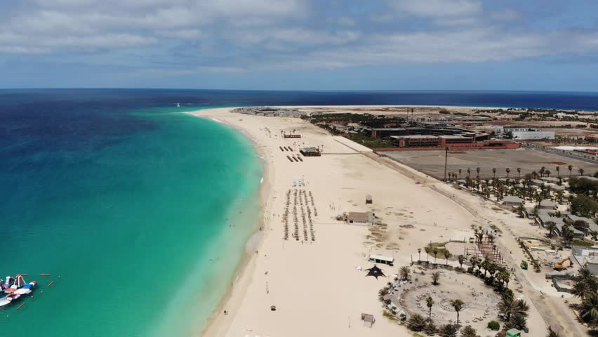 Aerial footage of the beautiful beach and coastline of Cape Verde (Capo Verde) with people sunbathing on the golden sandy beach and boasts in the ocean, taken with a drone on a beautiful day.