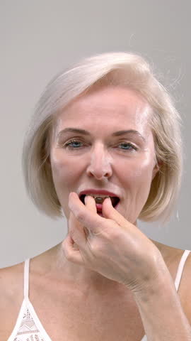 Old woman holds a yellow capsule or medicine tablet in her hand. Senior female takes dietary supplements, puts the drug or pill in her mouth. Lady takes care of the beauty of the body, rejuvenation