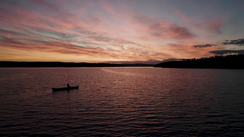 A lone canoe on a calm lake at sunset in Sweden, silhouetted against a vibrant sky