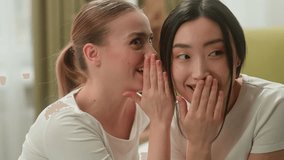 Multiracial friends women Caucasian woman whisper secret gossip talk secrecy information on ear to Asian Japanese female Chinese Korean girl laughing smiling talking confidential gossiping indoors - Powered by Shutterstock - Get 15% off with code: PIKWIZARD15