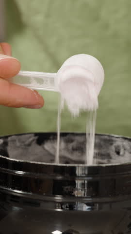 Vertical video. Man Showing White Powder in a Black Jar with a Measuring Spoon Inside. Sports Supplement Creatine.