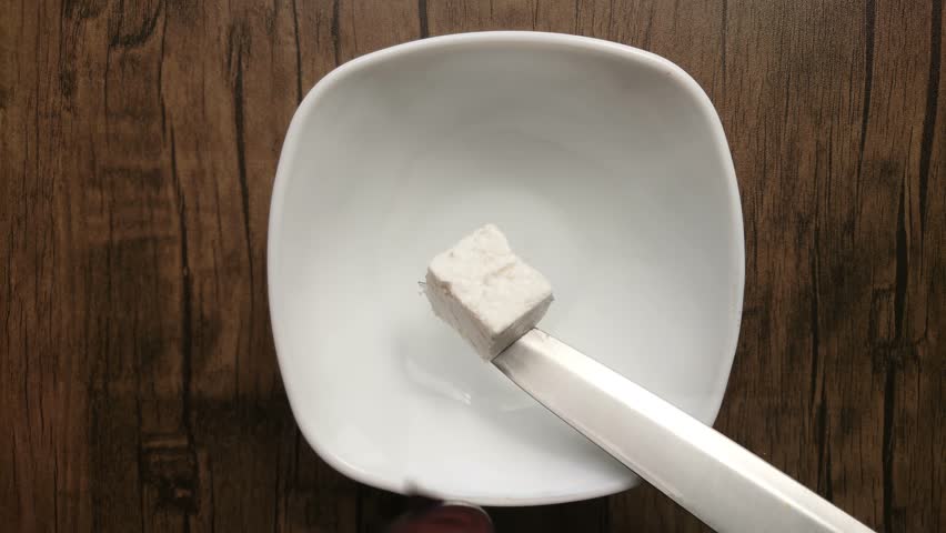 Top view of soft feta cheese cube placed into white bowl with the kitchen knife . High quality 4k footage