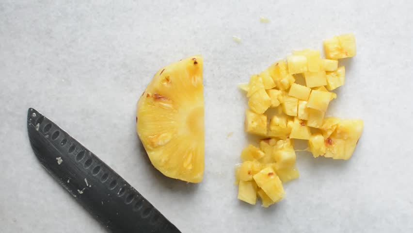 Top view of pineapples being diced on a marble countertop, overhead view of chopped pineapples on a white background