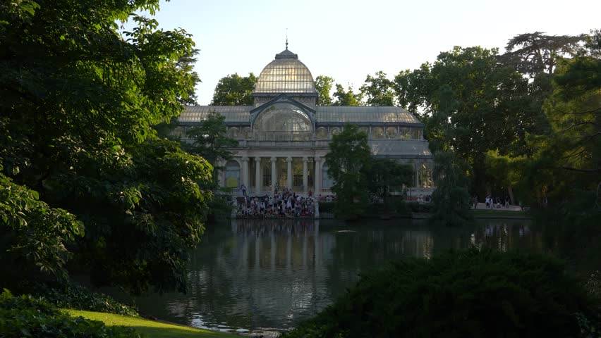 Wide View Glass Palace in Madrid Spain Daylight Crowd Sits On Steps. Palacio de Cristal. Famous Landmark Retiro Park European Destination