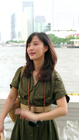 Young Asian woman backpack traveler wearing a hat at express boat pier on Chao Phraya River in Bangkok. Journey trip lifestyle, world travel explorer or Asia tourism concept. Vertical footage..