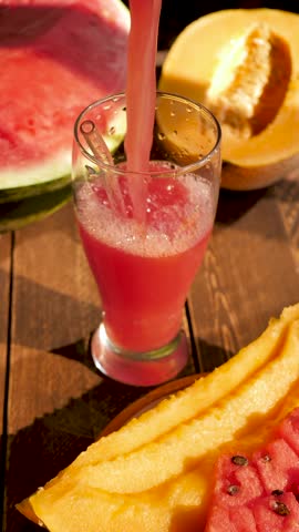 Vertical: Red watermelon juice pouring into drinking glass and reusable glass straw. Refreshing cocktail mixed watermelon and melon. Fruit smoothie watermelon and melon. Summer menu