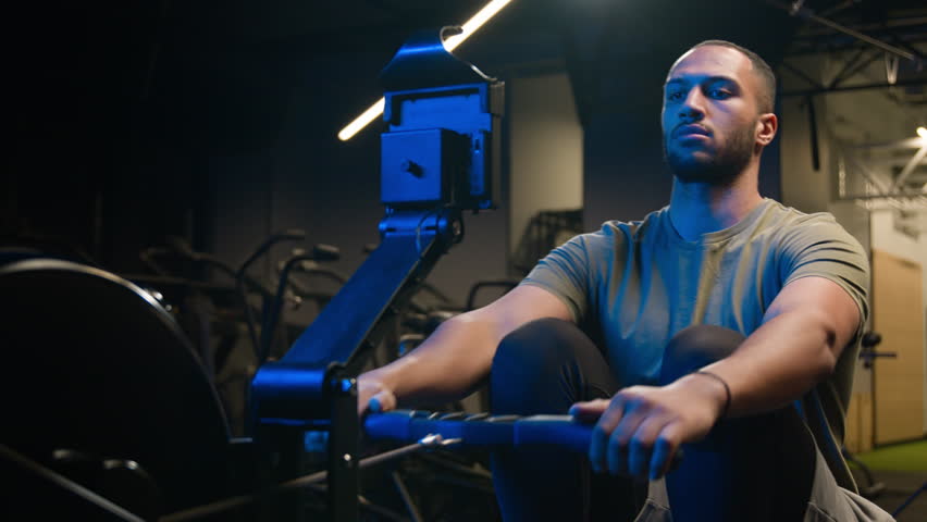 Sport determination hard exercise with equipment in sportive club muscles workout African American strong man sporty male guy athlete sportsman bodybuilder in gym pulling rope rowing machine sitting