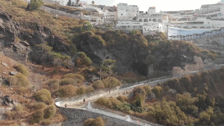 Aerial panorama drone view from above of path road from the port to the top which can be walked or ridden by horse or donkey. Fira, Santorini Island, Greece. Thira city. Aegean Sea, Mediterranean.
