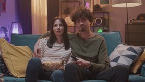 Loving couple watching horror movie on TV. Attractive man hugging his girlfriend while watching television at home. Beautiful woman holding plate full of popcorn while sitting with her male on sofa. - Powered by Shutterstock - Get 15% off with code: PIKWIZARD15