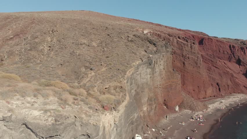 Aerial panorama drone view of Red beach in Santorini in Akrotiri region, Greece. Red rock cliff and beach with water on the sea. Aegean Sea, Mediterranean. From above
