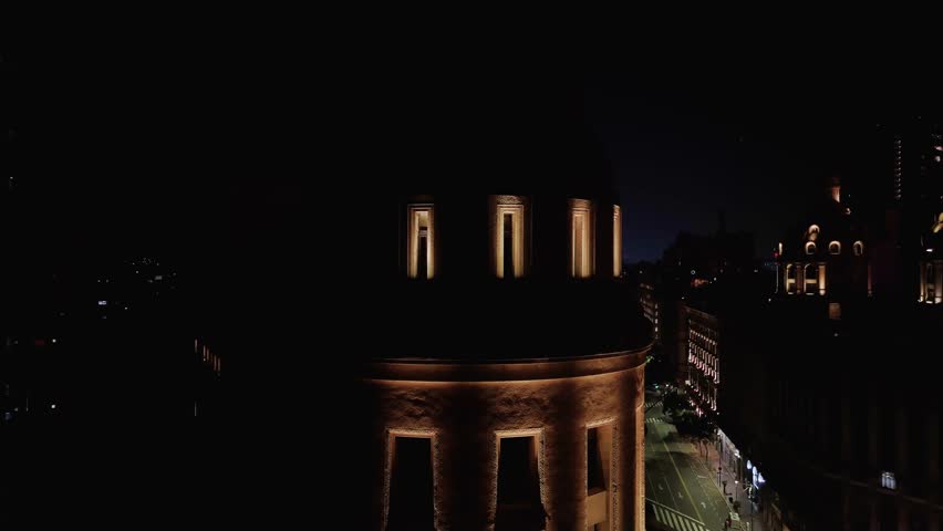 Illuminated old dome and Obelisk of Buenos Aires at night. Aerial camera surrounds the dome and reveals the obelisk in the background