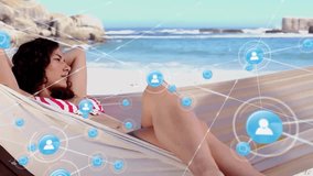 Animation of network of connections with icons over biracial woman lying in hammock on beach. Global connections, vacations, summer, lifestyle and digital interface concept digitally generated video. - Powered by Shutterstock - Get 15% off with code: PIKWIZARD15
