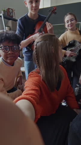 Vertical shot of young school teacher taking selfie with five elementary students holding musical instruments after music lesson