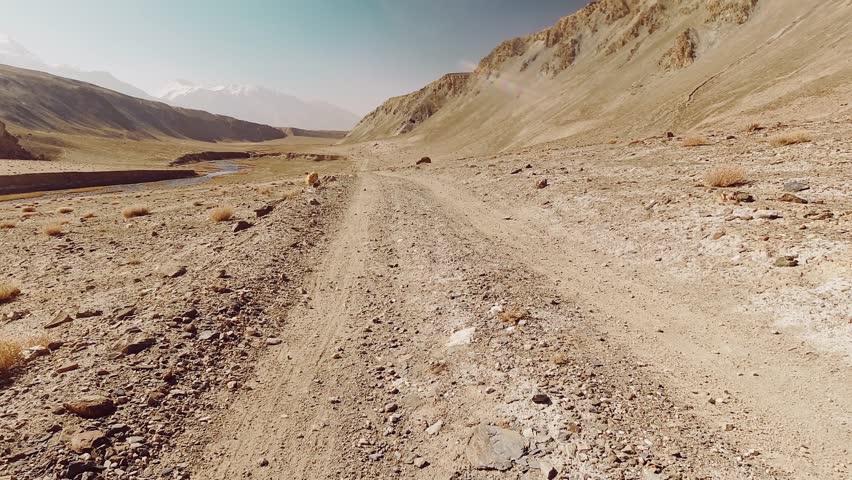 Fast motion hyper lapse biking curvy turning gravel bumpy road section with beautiful Pamir mountains background. Bartang valley in Pamir highway route. Touring explore and travel concept background