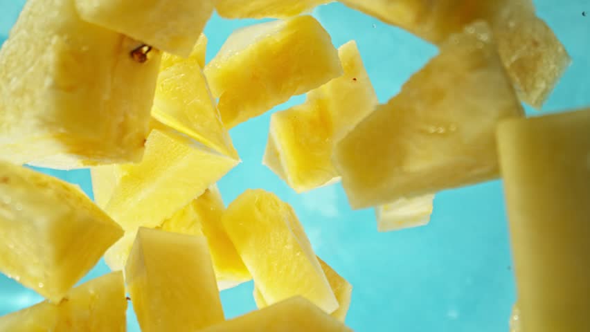 Super Slow Motion of Falling Pineapples Slices into Water, Blue Background. Filmed on High Speed Cinema Camera, 1000 fps. Camera Tracking the Target.