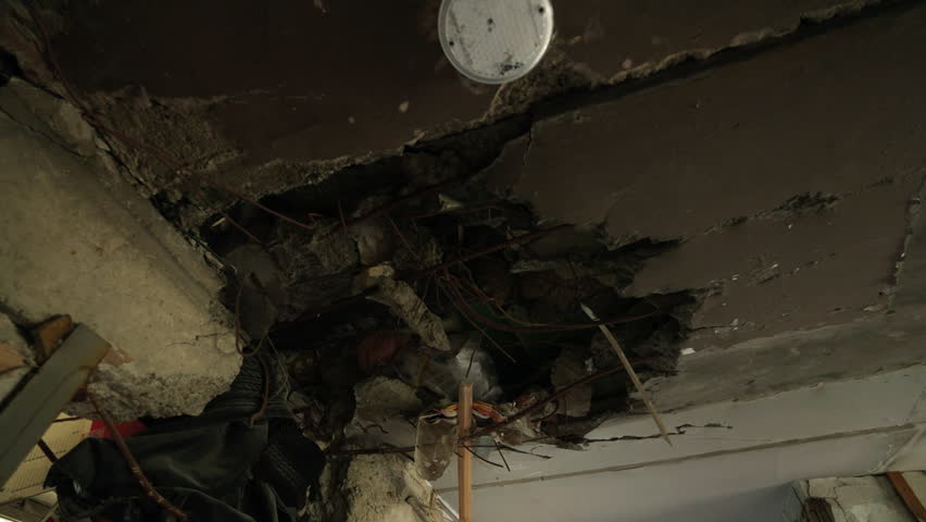 Exposed wires, shattered concrete in Mariupol apartment ceiling after shell hit. Destruction, exposed infrastructure in war impact zone, building interior damage evidences. Slow motion.