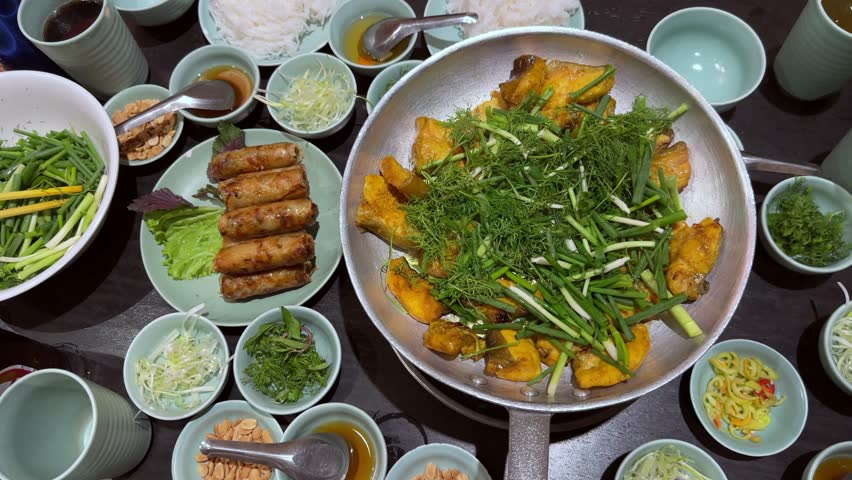 Vietnamese fried spring rolls Nem Ran, with a dish of boneless grilled hemibagrus fish, river catfish fried called Cha Ca La Vong Hanoi, table of diners with fresh dill and spring onion, cilantro