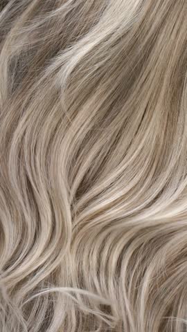 Close-up blond curly hair texture, vertical long hair background in slow motion