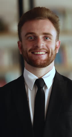 Thoughtful handsome young Caucasian businessman wearing formal suit and tie, looking at camera, getting happy, positive, smiling. Male CEO, executive, business leader vertical head shot portrait