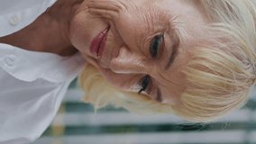 Smiling pensioner relaxing at street in white shirt close up. Portrait of happy retired woman looking down reading message outdoors vertical video. Elegant senior lady sitting urban area enjoy weekend - Powered by Shutterstock - Get 15% off with code: PIKWIZARD15