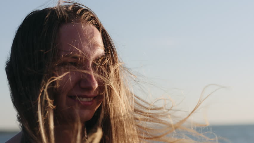 Slow motion closeup portrait of young girl standing on a beach and wind blows her hair