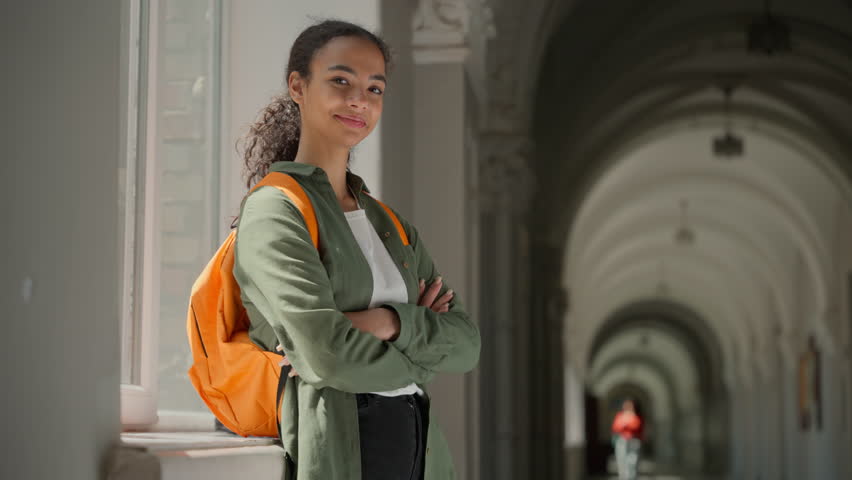 Portrait happy smiling confident Hispanic woman student girl Latina female lady in school university college academy hall corridor stand posing crossed hands looking at camera education exam studying
