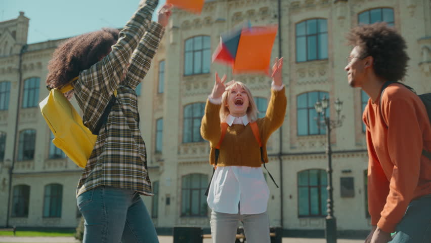 Multiracial friends students African man guy male Caucasian women girls females outdoors university high school throw copybooks air happy holidays end of session graduation passed exams success laugh