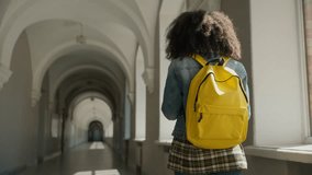 Back view from behind African student girl female schoolgirl woman lady walking in empty corridor hallway college high school university hall walk go move going to class schoolbag education study - Powered by Shutterstock - Get 15% off with code: PIKWIZARD15