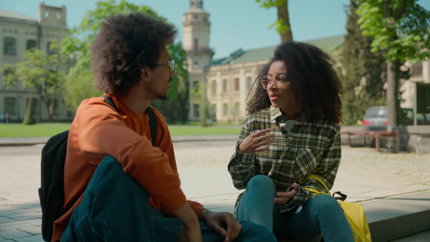 African American ethnic couple students people pupils classmates woman girl lady female man male guy sit outdoors in city talking friendly communicate conversation talk university college high school