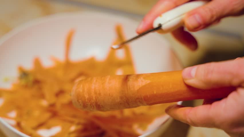 Close-up of female hands peeling fresh juicy carrot by peeler on the cutting board