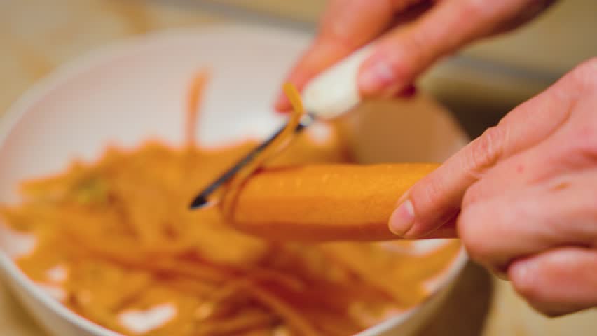 Close-up of female hands peeling fresh juicy carrot by peeler on the cutting board