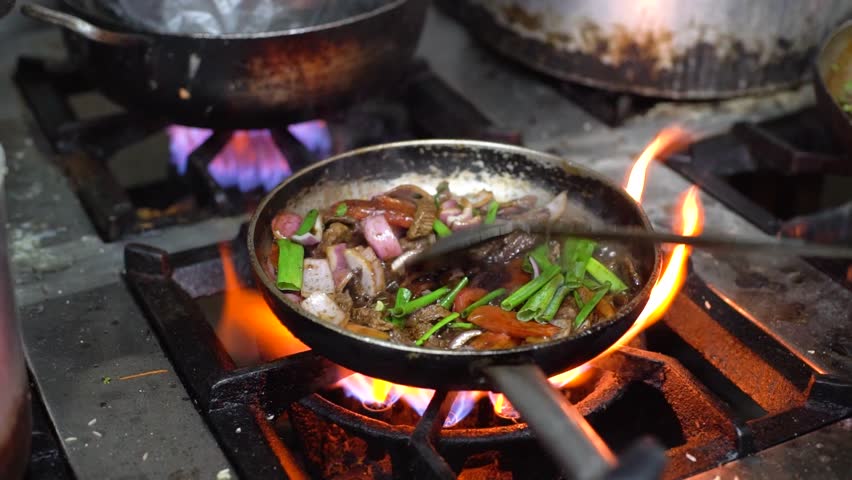 The frying pan on the fire with meat and vegetables inside