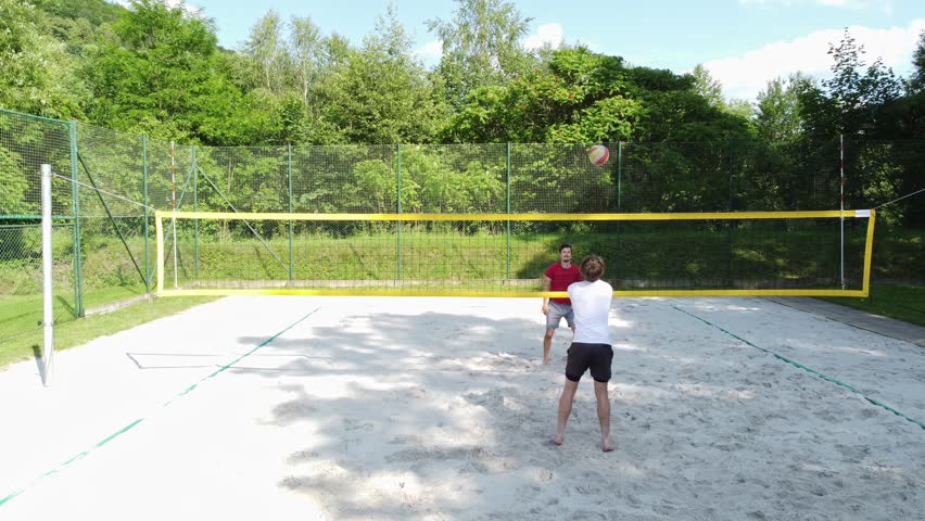Young volleyball players play beach volleyball on an outdoor beach court. Digging, hitting, blocking and passing training. Volleyball during a sunny day.
