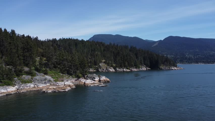 A drone shot of mountain forest of pine trees and deep blue sea water in Lighthouse Park, Vancouver, British Columbia, Canada