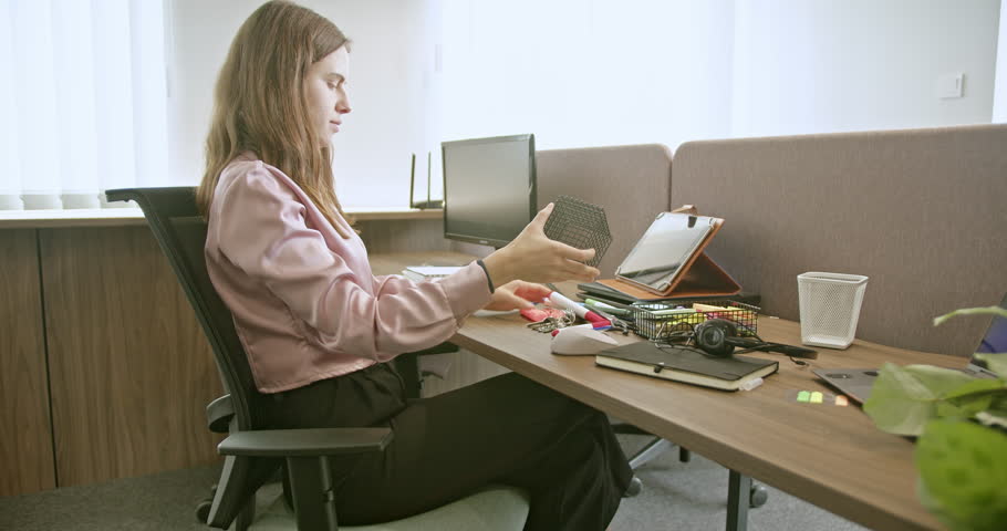 A young woman arranges office supplies at her desk in a modern workspace, utilizing stationery and getting ready for work in a professional setting.