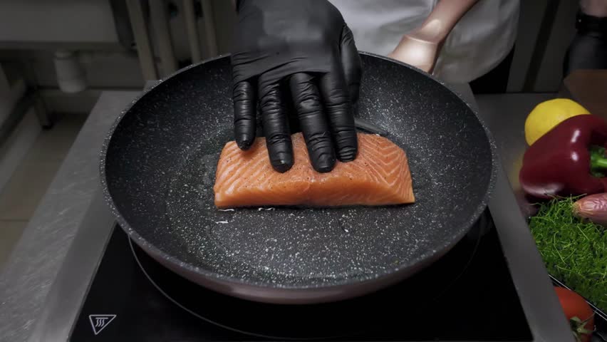 A man fries salmon fish with spices in a frying pan