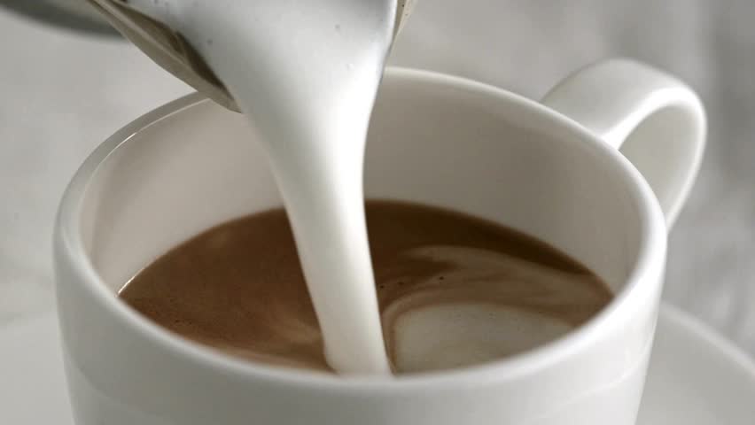 Latte art being made. Closeup video of coffee latte art making at cafe. Milk being poured into a white mug with coffee, creating a beautiful latte art.