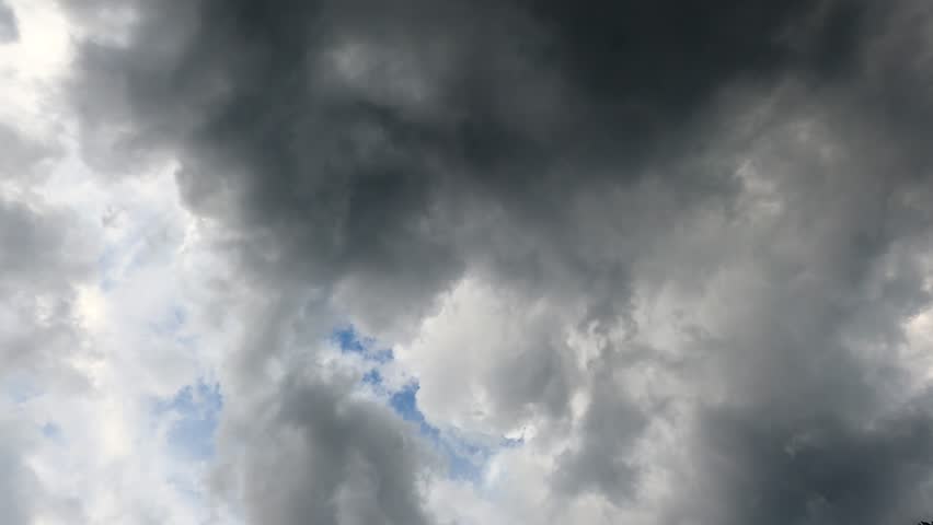 A low angle timelapse footage of dense gray stormy clouds floating in the blue sky in daytime