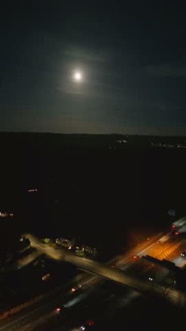 A vertical night view of beautiful full moon lighting the sky over the city