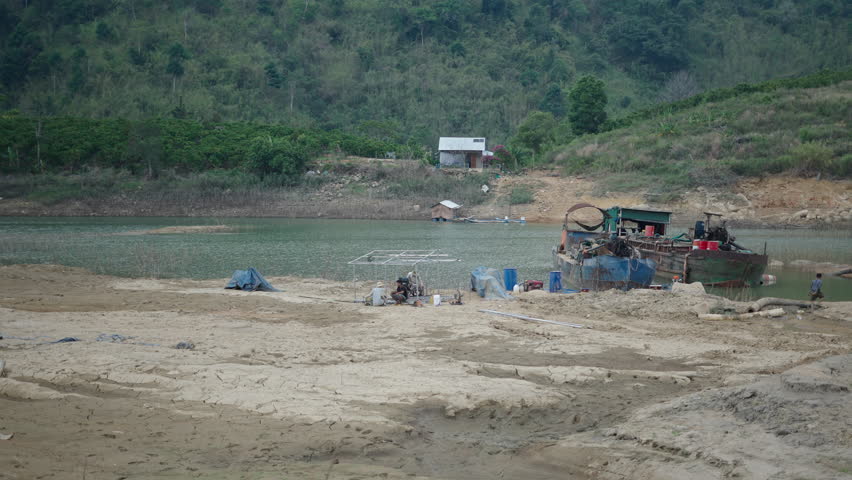 Boat mechanics on the bank of the river lake next to two old antique boats in Vietnam