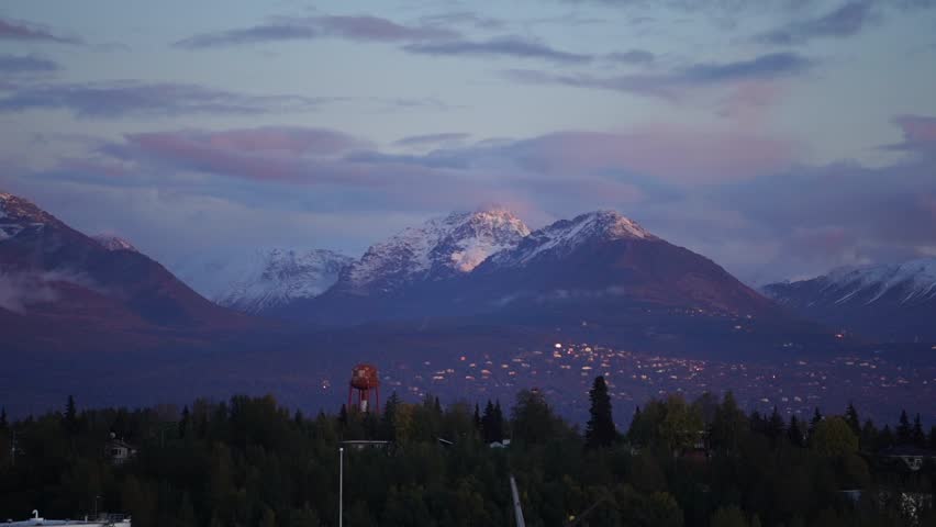A drone of dense trees and snowy peak under cloudy sky at sunset time in Anchorage city, Alaska