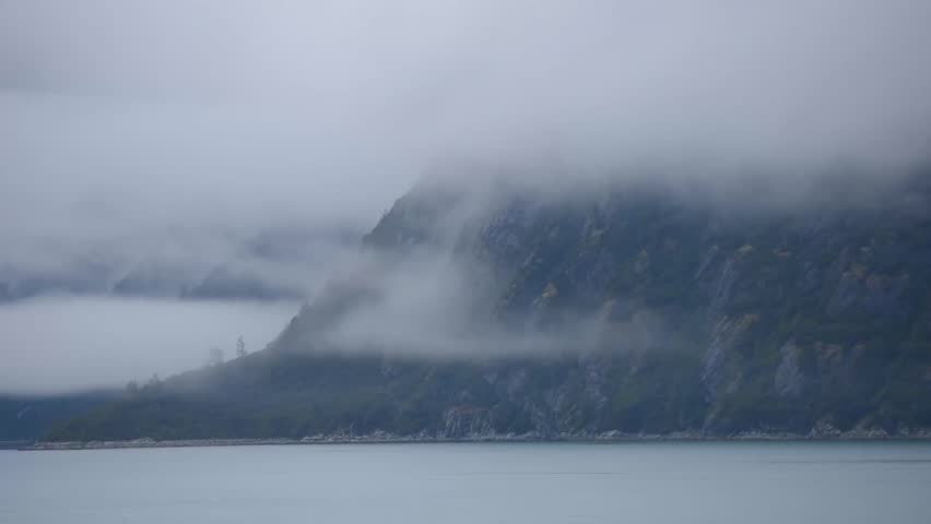 A drone shot of the rocky mountains covered with fog surrounding the Glacier Bay Basin, Alaska, USA